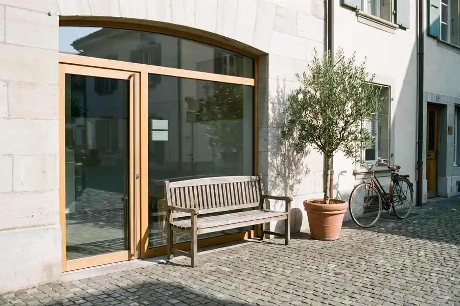 L'entrée du cabinet : porte vitrée de plain-pied dans une façade de pierre claire, un banc et un olivier.