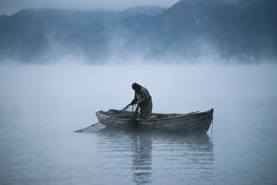 Un pêcheur relève son filet depuis une barque, sur le Léman dans la brume du matin.